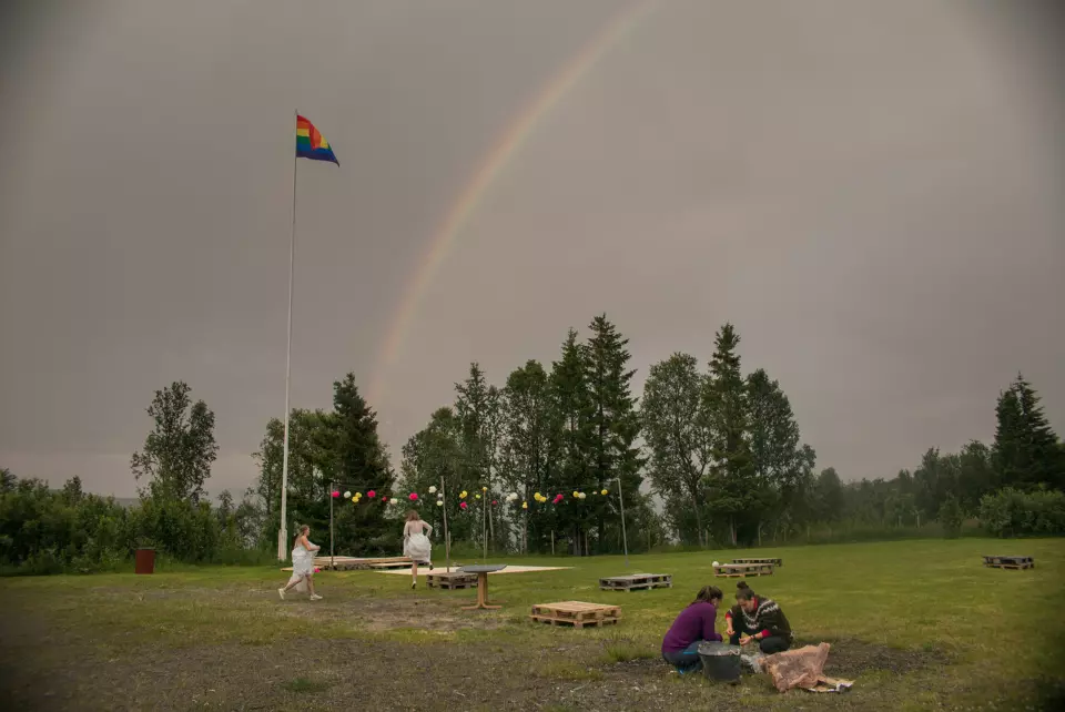 Regnbueflagget vaier under en dobbel regnbue i Lyngen. Brudeparet spretter ørville rundt. Foto: Annemor Larsen