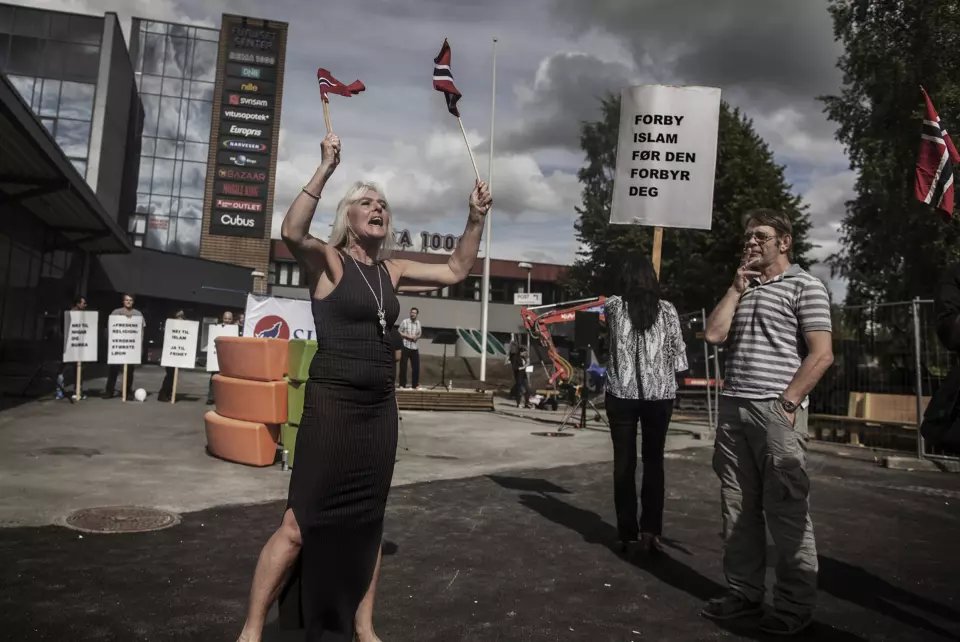 Anna Bråten vifter med norske flagg og roper mot flere hundre motdemonstranter. De har møtt fram for å vise sin avsky mot henne og organisasjonen SIAN – Stopp Islamifiseringen av Norge - på Furuset i Oslo. Foto: Espen Rasmussen
