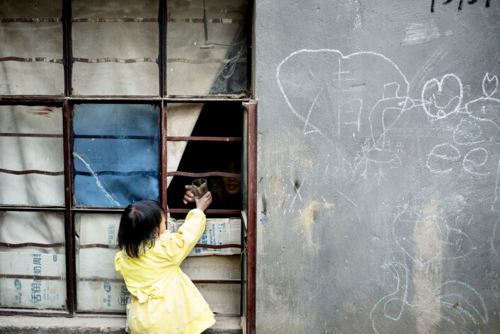 Enya Wu (4 1/2) får et glass vann av moren gjennom vinduet. På veggen ved siden av har noen tegnet et hjerte og skrevet «vær så snill», på kinesisk. Foto: Evelyn Pecori