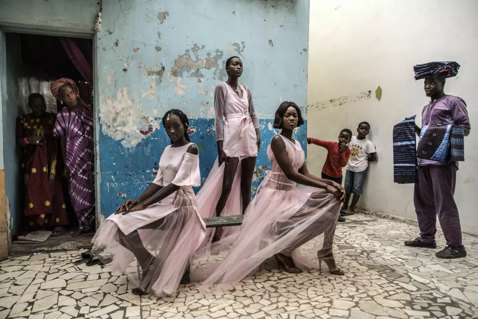 Diarra Ndiaye, Ndeye Fatou Mbaye og Mariza Sakho står som modeller for antrekk av designer Adama Paris, i Medina-området i Senegals hovedstad, Dakar, mens nysgjerrige innbyggere ser på. Foto: Finbarr O'Reilly