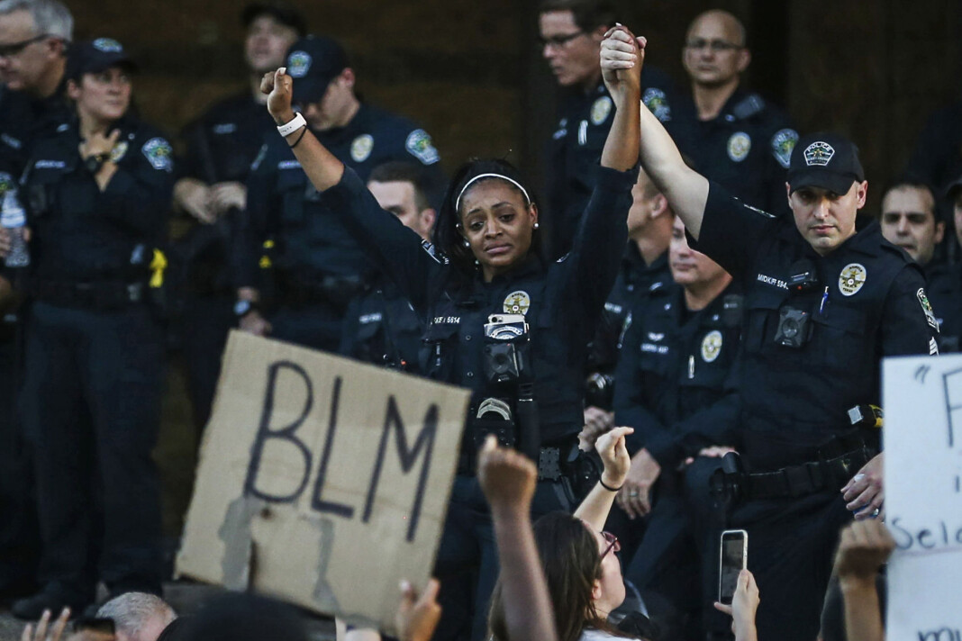 Politibetjent Alexandra Parker holder hendene til en kollega foran demonstranter i Austin fredag. Politibetjent Alexandra Parker holder hendene til en kollega foran demonstranter i Austin fredag.
