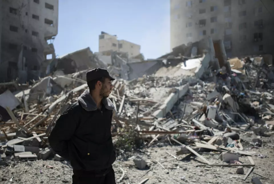 En palestinsk politimann står ved ruinene av høyhuset der en rekke internasjonale medier hadde sine kontorer i Gaza by. Høyhuset ble lagt i grus i et israelsk bombeangrep lørdag.