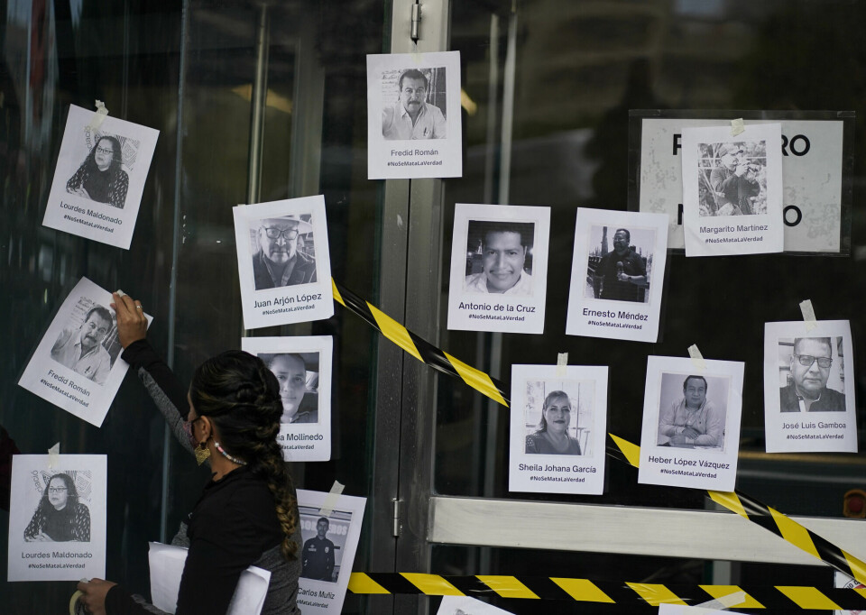 En mann henger opp bilder av journalister drept i Mexico under en demonstrasjon i august i fjor.
